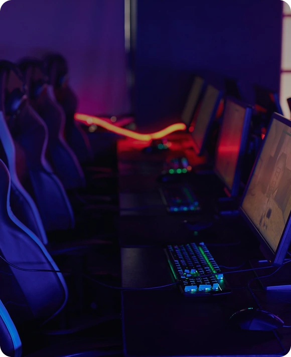 Een rij gamingcomputers met verlichte toetsenborden en stoelen in een esports-club, klaar voor spelers en wedstrijden.