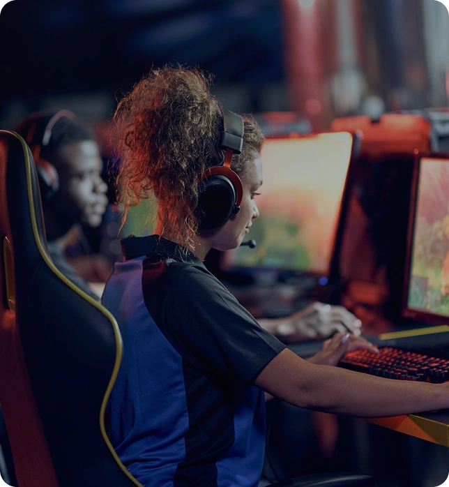 Een jonge speler zit achter een gamingcomputer met headset en traint geconcentreerd in een esports-omgeving met verlichte schermen.