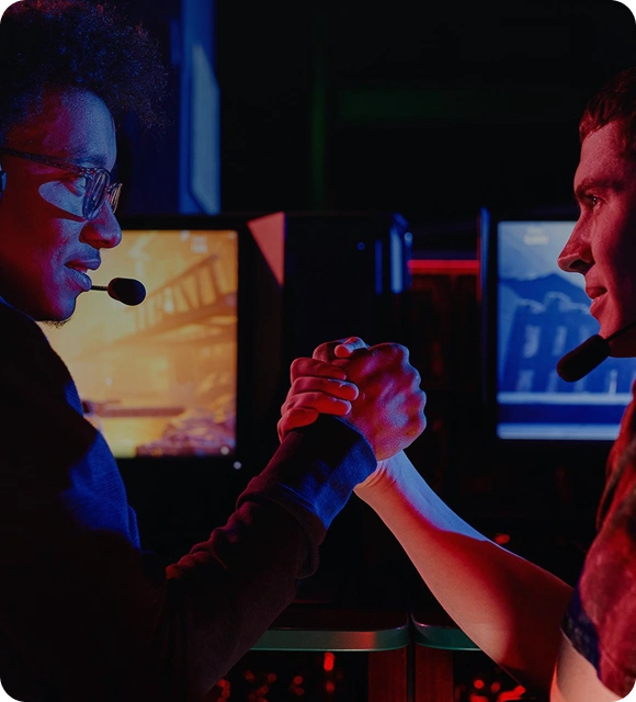 Twee spelers geven elkaar een hand in een esports-omgeving, terwijl gamingcomputers op de achtergrond zichtbaar zijn.