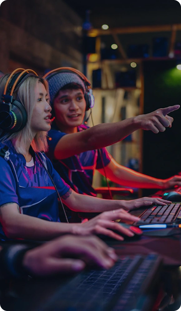 Twee spelers zitten naast elkaar achter gamingcomputers en spelen samen, terwijl ze communiceren en samenwerken tijdens een game.